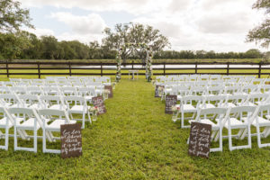 Outdoor Rustic Chic Wedding Ceremony with Love Quotes Hand Painted in White on Wooden Board, with Babys Breath and REd Floral in Hanging Mason Jars and White Folding Chairs, and Floral Ceremony Arch | Tampa Bay and Hillsborough County Farm Wedding Venue Wishing Well Barn