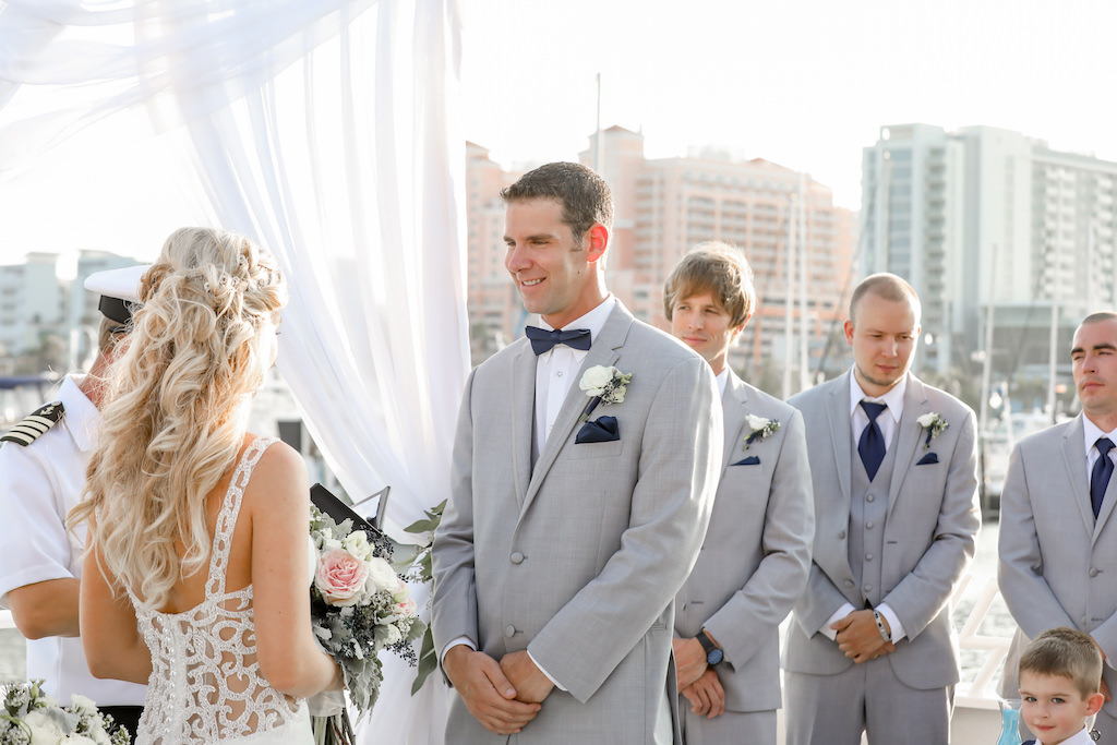 Outdoor Waterfront Wedding Ceremony Portrait, Groomsmen with White Rose with Blue Berry and Greenery Boutonniere, Navy Bow Tie and Pocket Square, and Light Gray Linen Suits, Bride in Lace Illusion Back Dress with Blush Rose Bouquet | Tampa Bay Wedding Photographer Lifelong Photography Studios | Clearwater Beach Unique Wedding Venue Yacht Starship