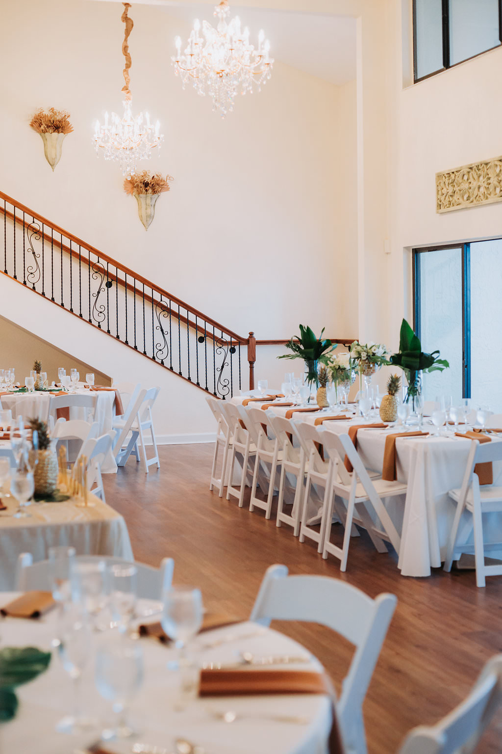 Indoor Hotel Ballroom Wedding Reception with Tan and White Table Linens, Pineapple and Tropical Greenery Centerpieces, and White Folding Chairs | Tampa Bay Waterfront Venue Beso Del Sol