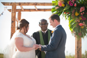 Outdoor Tropical Beach Wedding Ceremony Portrait with Bamboo Arch with Pink and Yellow Florals with Greenery, Bride in Capsleeve V Neck Lace Dress and Feather Hair Comb Veil Accessory, Groom in Gray Suit with Boutonniere | St Petersburg Wedding Photographer Caroline and Evan Photography