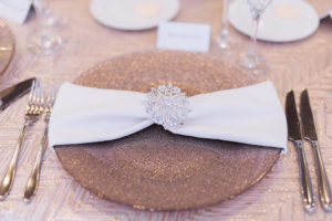 Elegant Wedding Reception Table Setting with Silver Snowflake Jeweled Napkin Ring on White Napkin on Gold Glitter Charger and Textured Linen | Tampa Bay Linens Over The Top Linen Rentals | Rentals Gabro Event Services