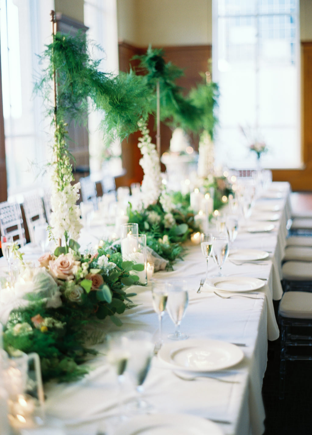 Hotel Ballroom White and Greenery Wedding Reception with Long Feasting Tables, Extra Tall White Spray and Garland Runner Centerpieces, with Ivory and Blush Roses and Clear Chiavari Chairs | Downtown Tampa Venue Le Meridien