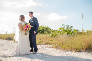 Outdoor Beach Wedding Portrait, Bride in Lace Cap Sleeve Dress with PInk and Orange Tropical Bouquet with Greenery and Striped Ribbon, Groom in Navy Suit with Boutonniere | St Pete Wedding Photographer Caroline and Evan Photography | Tampa Bay Wedding Dress Shop Truly Forever Bridal