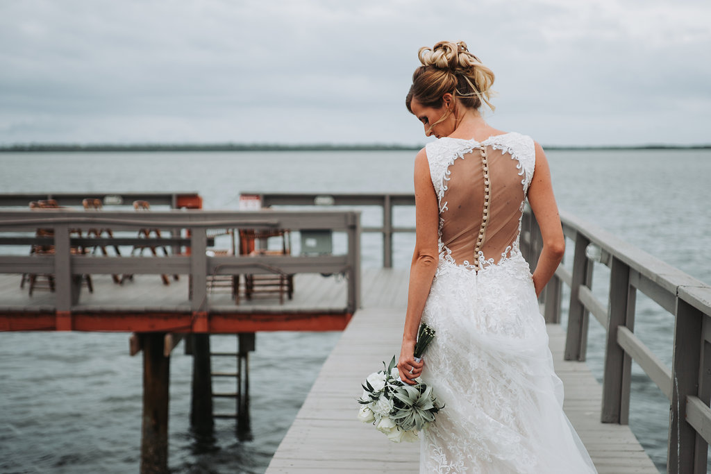 Outdoor Waterfront Bridal Portrait in Illusion Open Back Button Lace Dress with White Rose and Greenery Bouquet | Tampa Bay Wedding Photographer Grind and Press Photography | Dunedin Venue Beso Del Sol