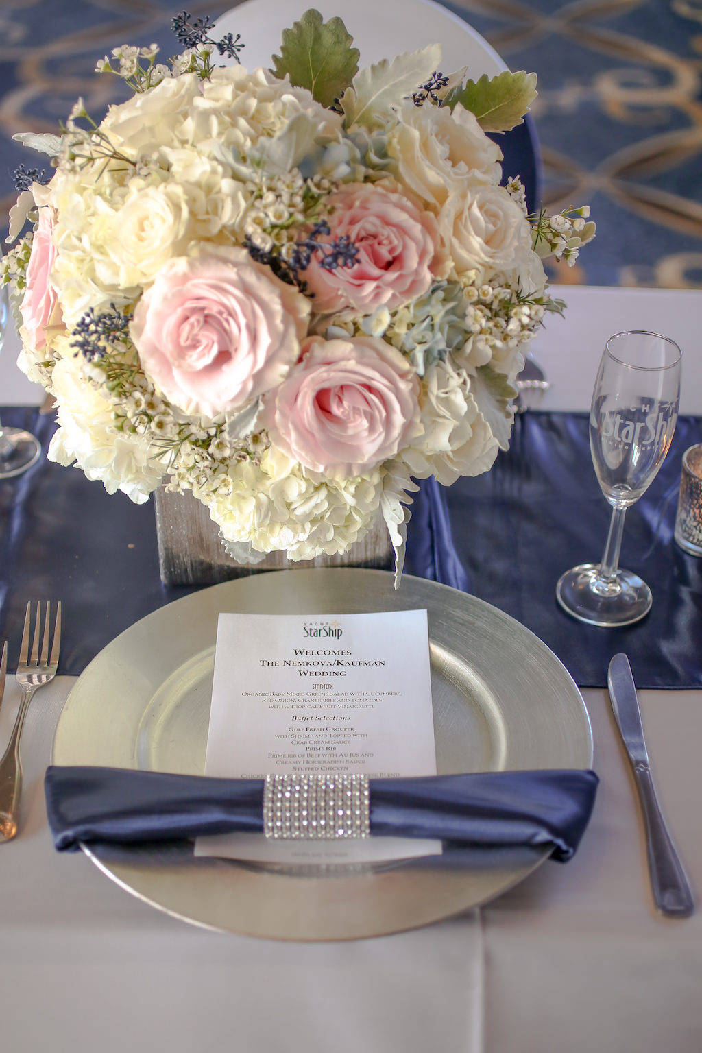 Nautical Wedding Reception Table Setting with Blush Pink and White Roses, Blue Berries and Greenery Low Centerpiece in Wooden Box, with Silver Charger, Navy Blue Linens and Satin Runner, Rhinestone Napkin Ring and Silver Charger | Tampa Bay Wedding Venue Yacht Starship