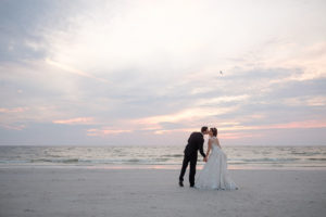 Outdoor Beach Sunset Wedding Portrait, Groom in Black Tux with Bow Tie and White Floral Boutonniere, Bride in Lace Cap Sleeve Belted A Frame Pronovias Dress | Tampa Bay Wedding Photographer Marc Edwards Photographs St Pete Beach Historic Hotel Wedding Venue The Don CeSar