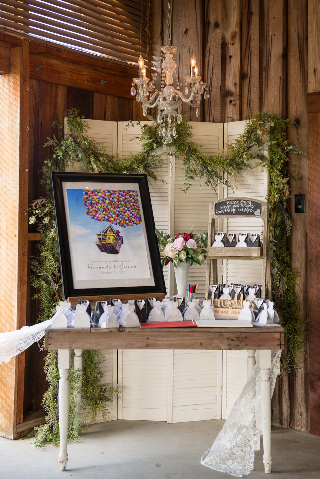 Barn Wedding Reception Favor Table with Framed Disney Up Movie Poster, and Black and White Favors, with Vintage Chandelier, Wooden Table, and Greenery Garland