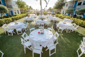Outdoor Hotel Courtyard Boho Tropical Wedding Reception with Round White LInen Tables and Folding Chairs, Small Pink Floral Centerpieces in White Ceramic Bowls and Gold Candlesticks | St Pete Beach Wedding Venue The Postcard Inn