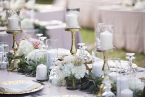 Outdoor Beach Wedding Reception with Blush Pink LInens, Gold Chargers and Candlesticks, Hurricane Lantern Candles and Greenery Garland Centerpiece with White Hydrangea Florals