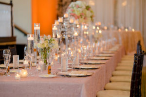 Hotel Ballroom Pink and Champagne Wedding Reception Long Feasting Table with Tall and Low Ivory and Pink Rose Centerpieces with Greenery, Floating Votive Candles in Glass Holders, Black Chiavari Chairs | Textured Linen Rentals from Kate Ryan Linens | Historic Waterfront Hotel Wedding Venue The Don CeSar