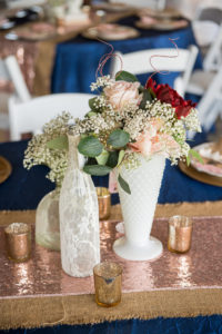 Rustic Barn Wedding Medium Height Centerpiece with Baby's Breath, Blush Pink and Red Rose with Greenery in White Glass Vintage Mismatched Vase and Bottles, with Burlap and Rose Gold Sequin Layered Runner and Navy Blue Linens