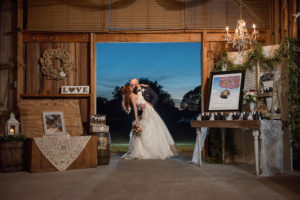 Bride and Groom Portrait at Barn Wedding Reception with Favor Table with Framed Disney Up Movie Poster, and Black and White Favors, with Vintage Chandelier, Wooden Table and dTrunk with Lace, Lantern, and Greenery Garland | Tampa Bay Venue Wishing Well Barn