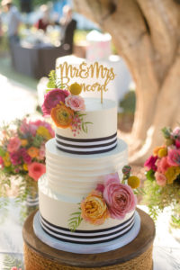 Three Tier Round White With Navy Blue Stripe Wedding Cake on Wooden Nautical Cake Stand with Stylish Custom Gold Caketopper with Pink and ORange Tropical Flowers with Ferns