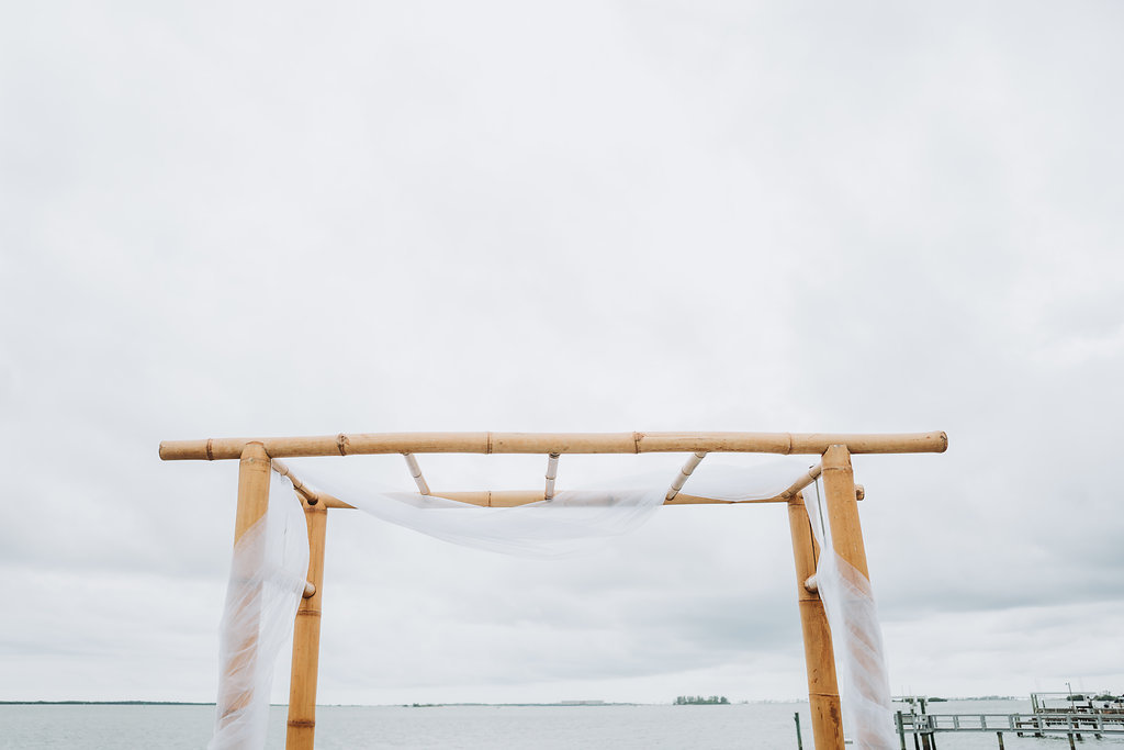 Simple Outdoor Waterfront Wedding Ceremony with Bamboo Arch with White Draping