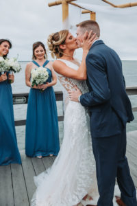 Outdoor Waterfront Wedding Ceremony First Kiss Portrait, Groom in Blue Suit, Bride in Lace Cutout Dress, Bridesmaids in Mismatched Blue Dresses with White and Succulent Greenery Bouquet | Tampa Bay Wedding Photographer Grind and Press Photography