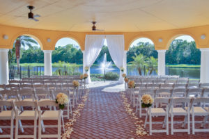 Outdoor Covered Courtyard Wedding Ceremony with White Draping Ceremony Arch, White Folding Chairs, Flower Petal Aisle and White and Blush Pink Floral with Greenery | Tampa Bay Wedding Rentals and Florist Gabro Event Services | Venue Tampa Palms Golf and Country Club