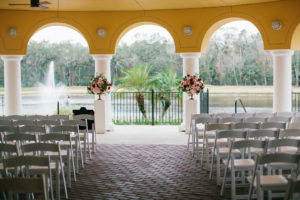 Outdoor Wedding Ceremony with Pink, Wine, and Red Rose Florals in Gold Vases on Pedestals and White Folding Chairs | Venue Tampa Palms Golf and Country Club | Planner Parties A La Carte