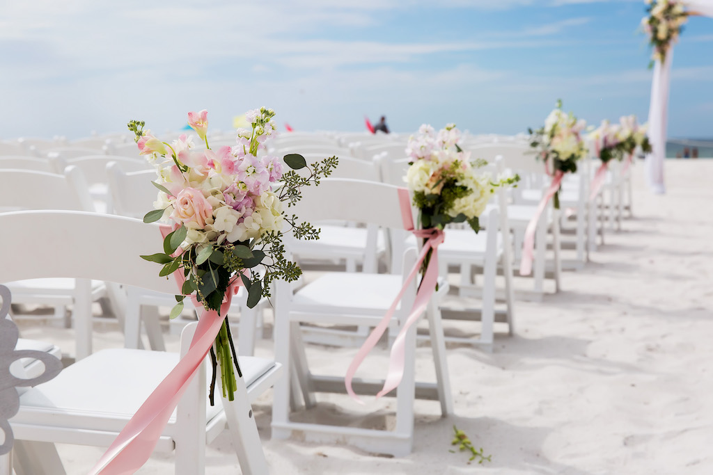 Outdoor Beach Wedding Ceremony decor with White Folding Chairs, White and Pink Floral with Pink Ribbon and Draping, Bamboo Ceremony Arch | Tampa Bay Waterfront Hotel Wedding Venue Hilton Clearwater Beach | Rentals A Chair Affair