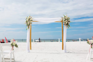 Outdoor Beach Wedding Ceremony decor with White Folding Chairs, White and Pink Floral with Pink Ribbon and Draping, Bamboo Ceremony Arch | Tampa Bay Waterfront Hotel Wedding Venue Hilton Clearwater Beach