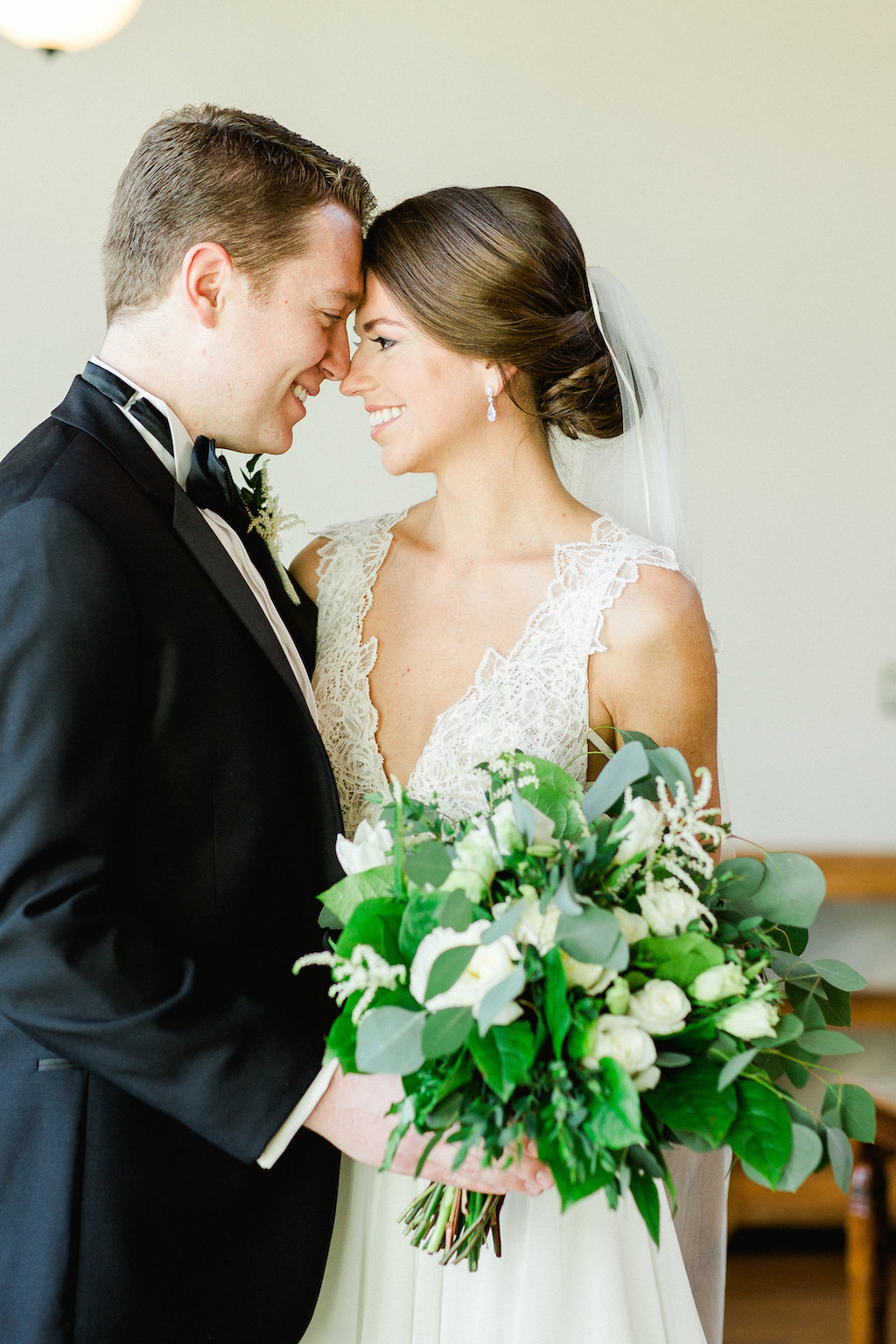 Indoor First Look Portrait, Bride in Lace V Neck Hayley Paige Dress, Groom in Black Tuxedo, with White Floral and Greenery Bouquet | Tampa Bay Wedding Photographer Ailyn La Torre Photography | Bridal Hair and Makeup Femme Akoi Beauty Studio