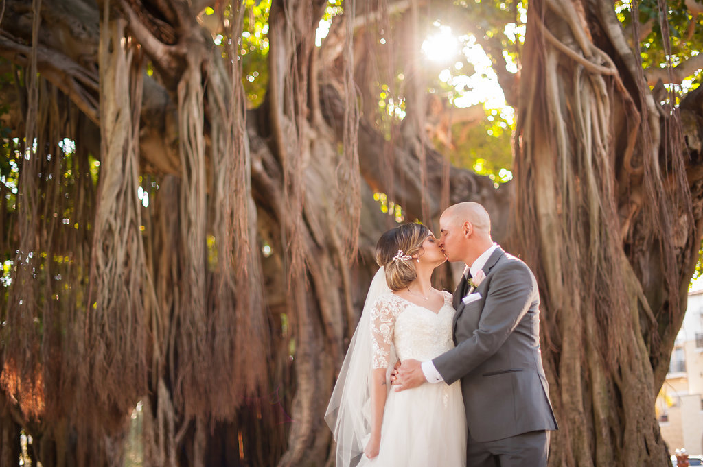 Outdoor First Look Wedding Portrait, Groom in Gray Suit with Blush Pink Rose and Greenery Boutonniere, Bride in V Neck Lace Sleeve David's Bridal Dress, with Banyan Trees | Downtown St Pete Wedding Ceremony Venue North Straub Park