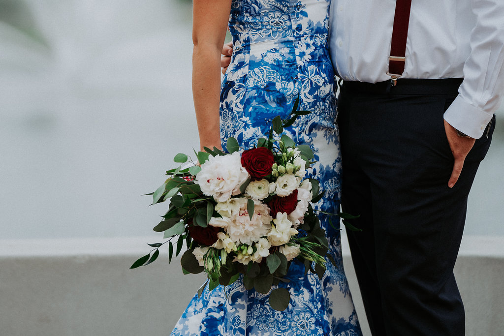 Outdoor Wedding Portrait, Bride in Strapless Blue and White Printed Dress with Red, White and Greenery Bouquet, Groom in White Shirt with Red Suspenders | St Pete Wedding Photographer Grind and Press Photography | Tampa Bay Florist Apple Blossoms Floral Designs