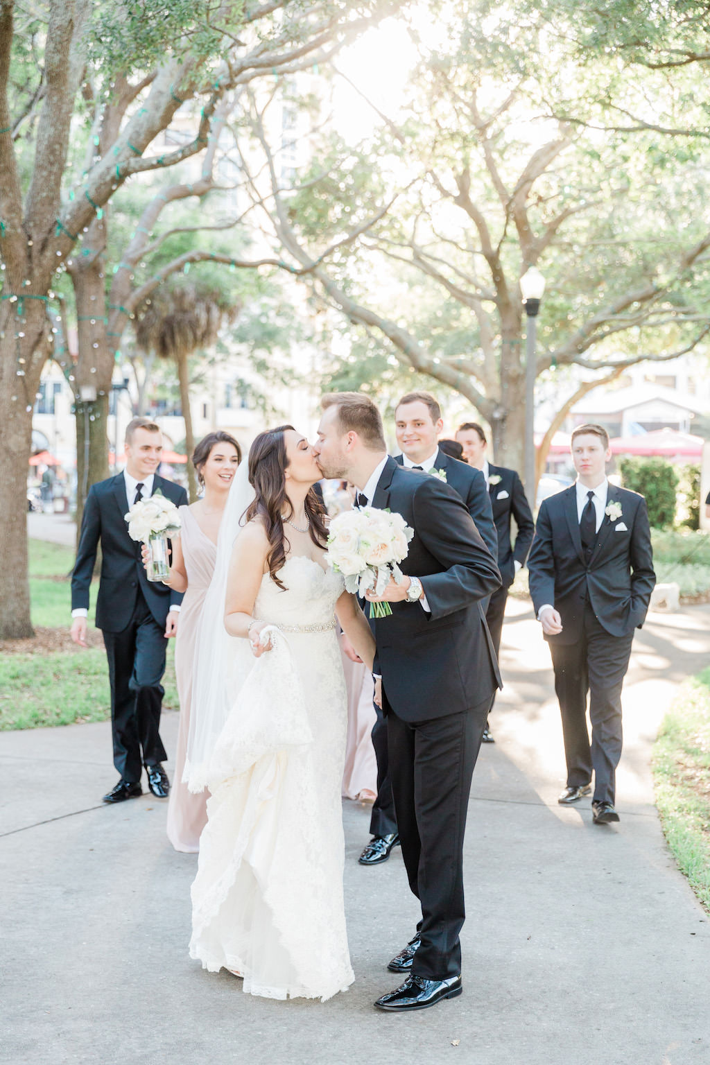 Downtown St. Pete Straub Park Wedding Party Portrait, Bride in Strapless Belted Column Dress, Groom and Groomsmen in Black Suits with White Floral Boutonniere, with White Rose Bouquet, Bridesmaids in Taupe | St Petersburg Wedding Florist Cotton and Magnolia