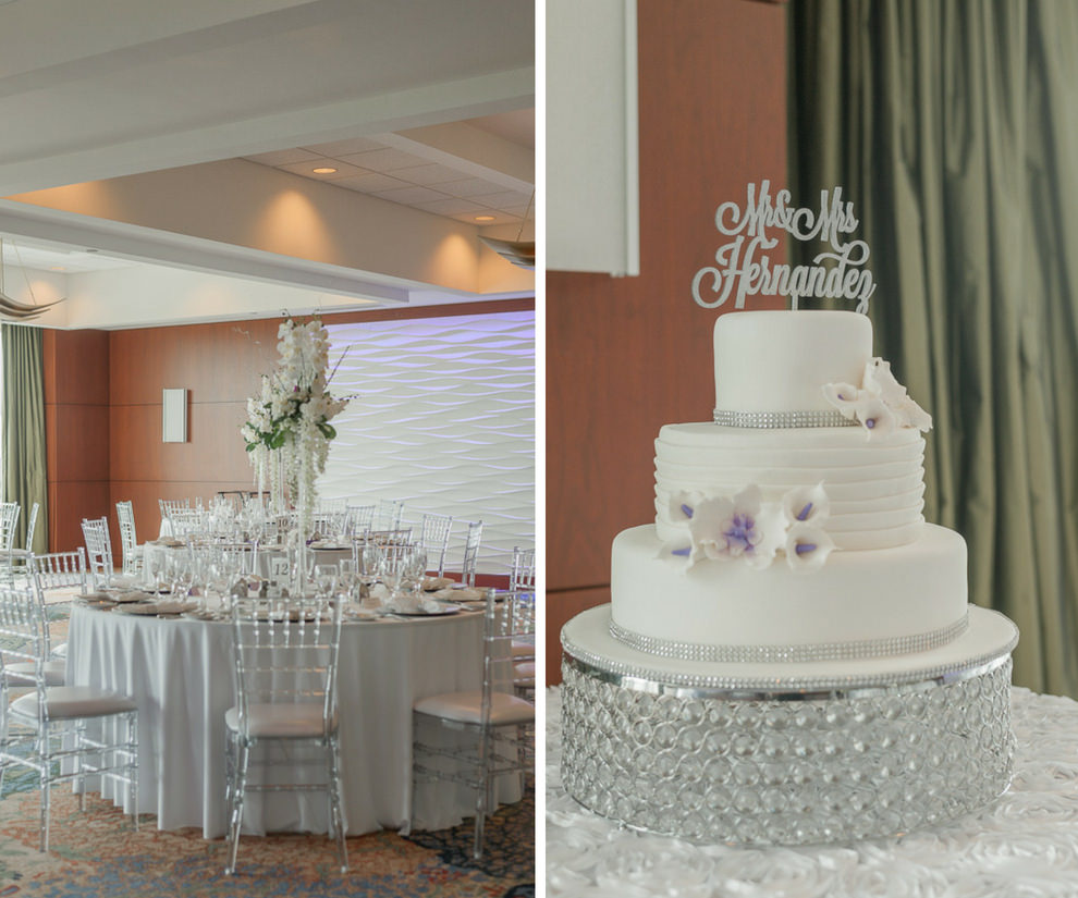 Three Tier Round White Wedding Cake with Silver Details, Custom Glitter Cake Topper on Glass Cake Stand with White and Lavender Flowers, and Indoor Hotel Ballroom Wedding Reception with Clear Chiavari Chairs, Round Tables, Silver Chargers, and Extra Tall Hanging White Floral with Greenery and Orchid Centerpiece | Tampa Bay Wedding Rental Company Kate Ryan Linen Rentals | Waterfront Venue Westin Tampa Bay
