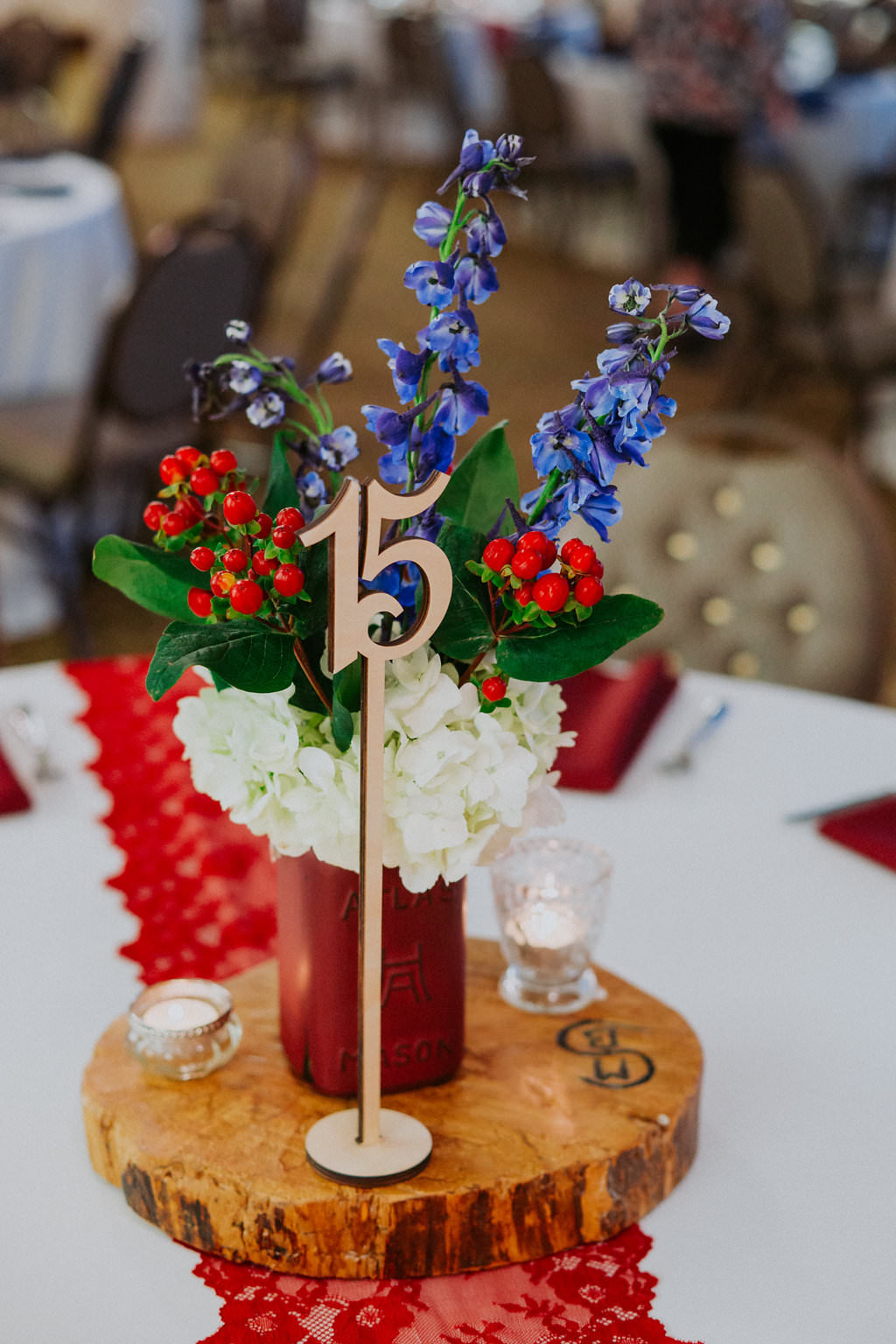 Americana Inspired Vintage Low Wedding Centerpiece with Blue and White Flowers and Red Berries with Greenery in Painted Vase on Natural Wood Round, with White Linens and Red Lace Runner and Laser Cut Wooden Table Number | Tampa Bay Wedding Planner Special Moments Event Planning | St Pete Florist Apple Blossoms Floral Designs