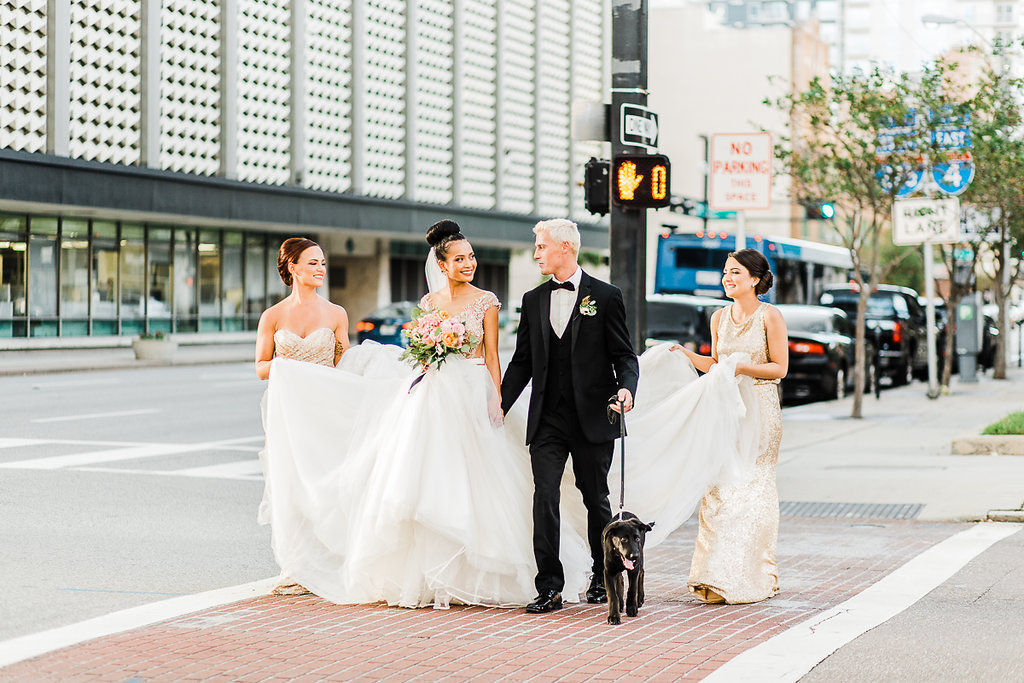 Outdoor Downtown Tampa Wedding Party Portrait, Bride in Ballgown Wedding Dress with Orange and Pink Floral with Greenery Bouquet with Black Ribbon, Groom in Black Tuxedo with Boutonniere, Bridesmaids in Mismatched Gold Sequin Dresses with Dog of Honor | Hair and Makeup Michele Renee The Studio