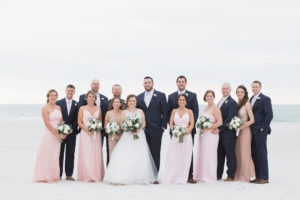 Outdoor Wedding Party Portrait at St. Pete Beach, Bridesmaids in Mismatched Blush Pink and Sequin Bella Bridesmaids Dresses, with White Floral and Greenery Bouquet with Ribbon, Groom and Groomsmen in Navy Blue Suits with Boutonniere and Satin Ties |Tampa Bay Planner UNIQUE Weddings and Events | Tampa Bay Planner UNIQUE Weddings and Events