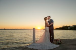 Romantic Sunset Waterfront Wedding Portrait, Bride in Lace V Neck Paloma Blanca Dress with Pink, White Floral and Anemone Bouquet with Natural Greenery, Groom in Gray Suit with Burgundy Red TIe and Succulent Greenery Boutonniere | Tampa Bay Wedding Photographer Andi Diamond Photography | Venue Palmetto Riverside Bed and Breakfast