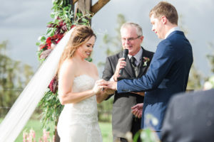 Outdoor Farm Wedding Ceremony Portrait, Bride in Sweetheart Strapless Lace Ines Di Santo Dress, Groom in Navy Blue Suit Men's Wearhouse Suit, with Wooden Ceremony Arch with Marsala Red Florals and Greenery