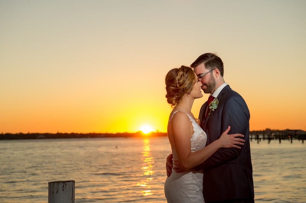 Romantic Sunset Waterfront Wedding Portrait, Bride in Lace V Neck Paloma Blanca Dress with Natural Greenery, Groom in Gray Suit with Burgundy Red TIe and Succulent Greenery Boutonniere | Tampa Bay Wedding Photographer Andi Diamond Photography | Venue Palmetto Riverside Bed and Breakfast