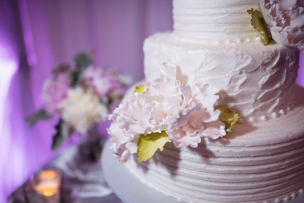 Three Tirered Round White Wedding Cake with Pink Paper Flowers with Gold LEaf Greenery and Pearls on Gray Cake Stand, with Satin Table LInens White Draping and Purple Uplighting