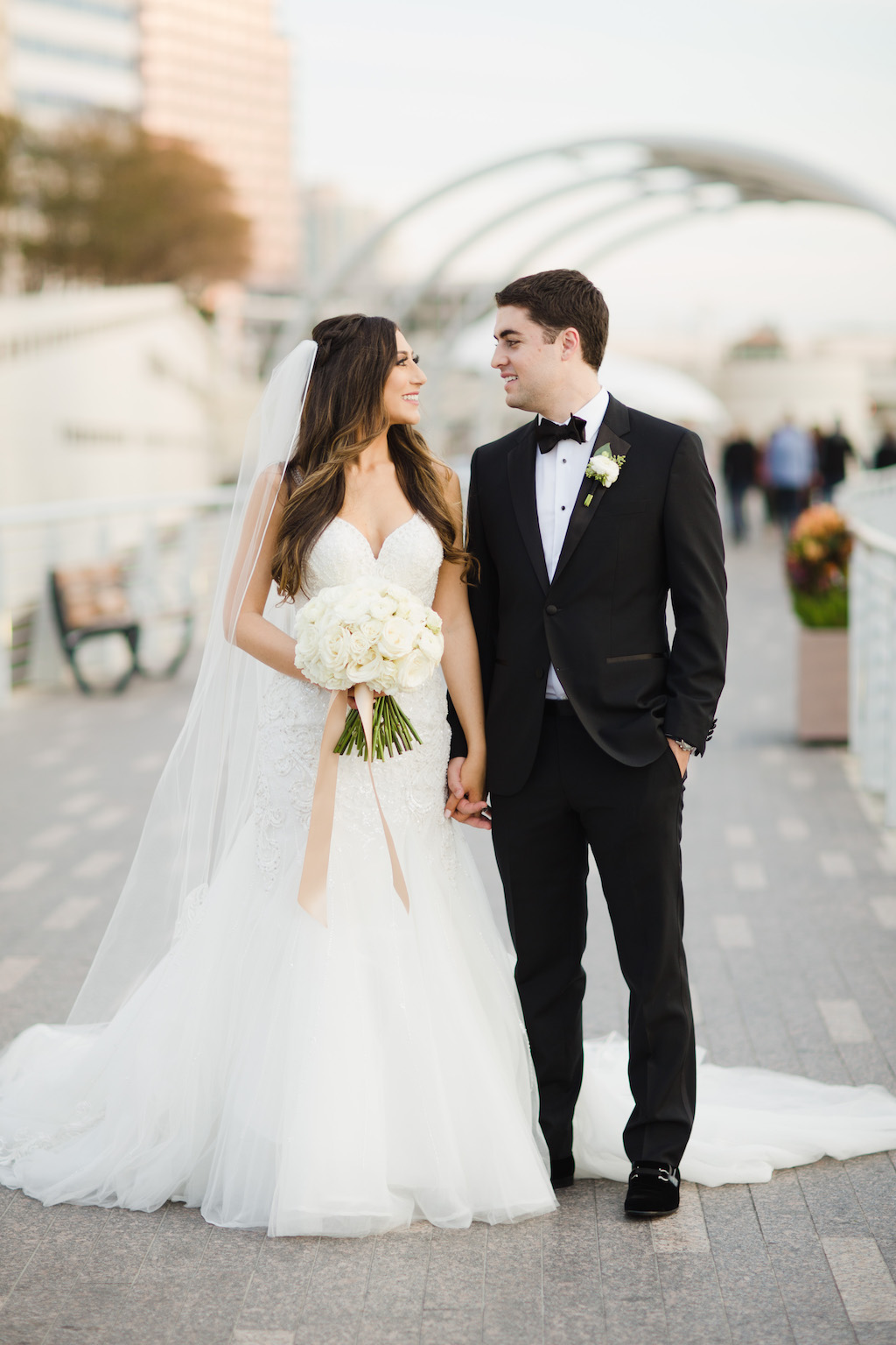 Downtown Tampa Riverwalk Outdoor Wedding Portrait, Bride in Princess Neckline Lace Trumpet Martina Liana Dress with Cathedral Veil, with White Rose Floral Bouquet with Champagne Ribbon, Groom in Black Tuxedo with Boutonniere