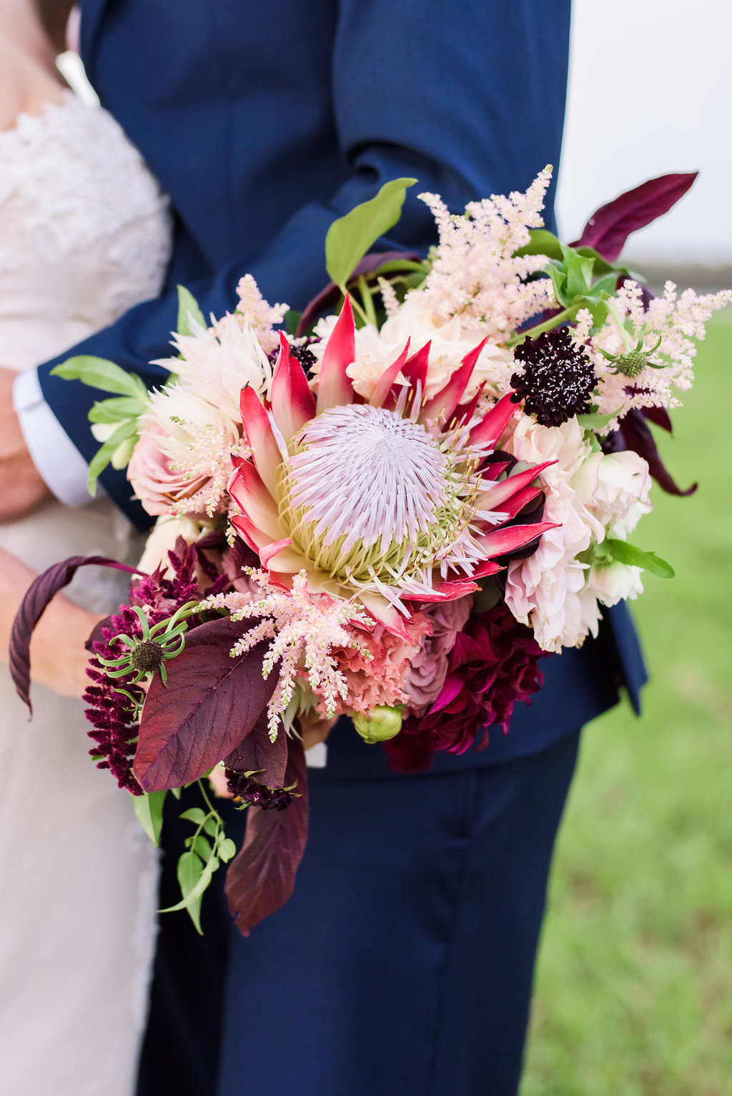 Outdoor Farm Wedding Bride and Groom Portrait, Groom in Navy Blue Suit, with Marsala Red Protea Bouquet with Greenery and BLush Pink Florals