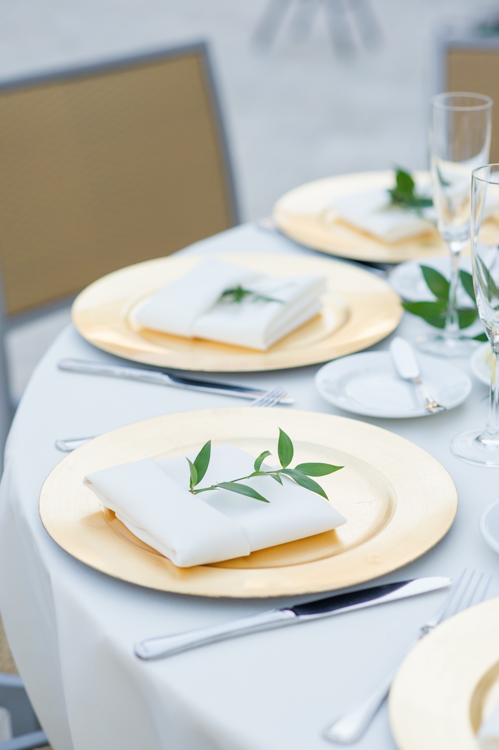 Simple Rustic Outdoor Wedding Reception Round Table Setting with Gold Charger, Silver Flatware, White Napkins and Linens with Greenery