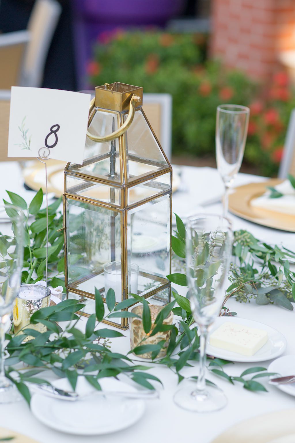 Simple Rustic Wedding Reception Round Table Centerpiece with Greenery, Vintage Gold and Glass Hurricane Lantern, and Handwritten Table Number on Printed Sage Card