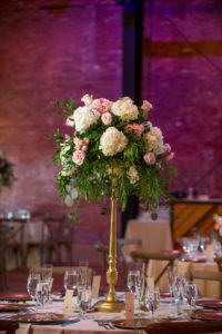 Industrial Chic Wedding Reception with Round Tables with Wooden Cross Back Chairs, Extra Tall White and Pink Rose Centerpieces in Gold Vases, Purple Uplighting and Blush and Ivory Linens | Exposed Brick Downtown Tampa Wedding Venue Armature Works