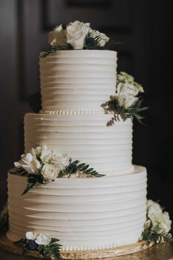 Three Tier Round White Wedding Cake on Flat Gold Cake Stand with White Rose and Greenery and Ferns