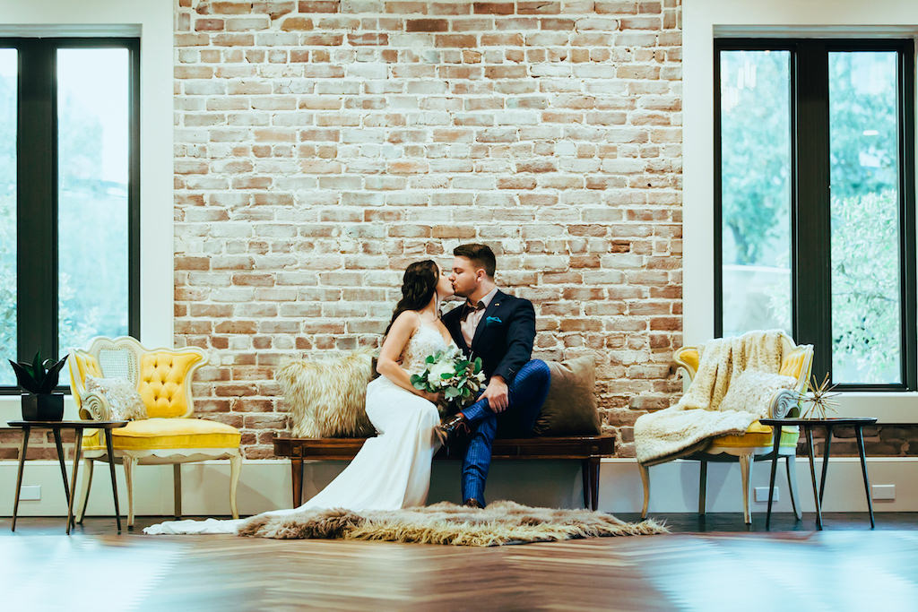 Indoor Modern Wedding Reception Lounge Portrait with Mustard Yellow Vintage Chair, Gray and fur Throw Pillows and Area Rug, and Succulent in Geometric Planter, Bride with Greenery Bouquet and Groom in Blue Suit with Blush Pink Shirt | Tampa Bay Wedding Planner Jennifer Matteo Event Planning | Downtown St Pete Exposed Brick Wedding Venue Red Mesa Events