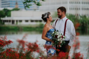 Outdoor Waterfront Downtown Wedding Portrait, Bride in Strapless Blue and White Printed Dress with Red, White and Greenery Bouquet and Birdcage Veil, Groom in White Shirt with Red Suspenders | St Pete Wedding Photographer Grind and Press Photography | Tampa Bay Florist Apple Blossoms Floral Desings