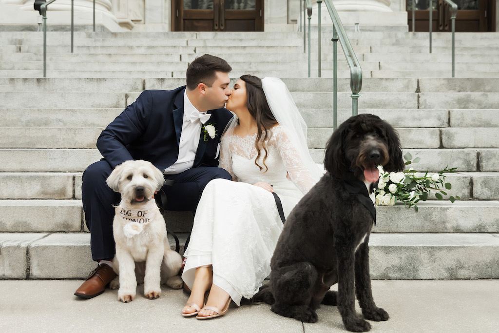 Outdoor Downtown Tampa Dog of Honor Wedding Portraits in Tuxedo and Lace Collar, Bride in Illusion Lace Long Sleeve Dress with Open Toed Wedding Shoes, Groom in Navy Blue Tuxedo with White Floral Boutonniere and Bow Tie | Tampa Bay Wedding Pet Coordinators FairyTale Pet Care