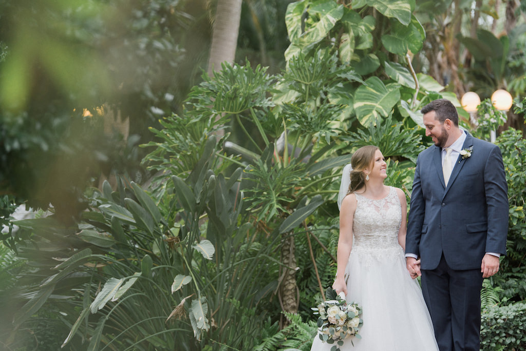 Outdoor Tropical Garden Wedding Portrait, Bride in Lace Illusion Ballgown Dress with White Floral and Greener Bouquet, Groom in Navy Blue Suit with Ivory Tie and Boutonniere