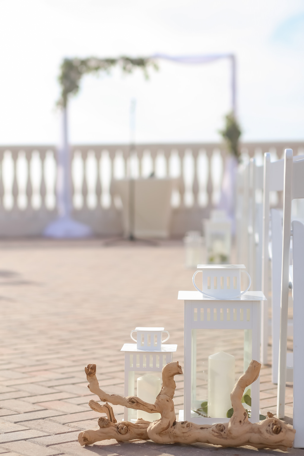 Outdoor Rooftop Coastal Wedding Ceremony Decor with White Hurricane Lanterns and Driftwood, and Greenery and White Draped Arch