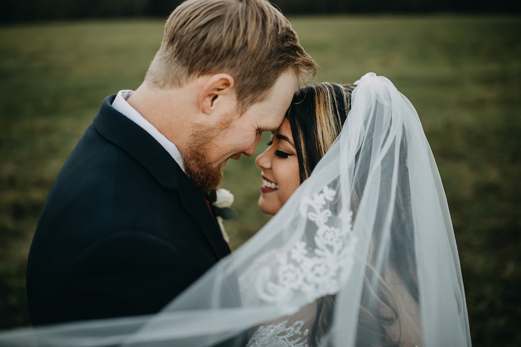 Creative Outdoor Wedding Portrait under Veil, Bride in Long Sleeve White Lace Wedding Dress, Groom in Navy Blue Suit with White Rose and Greenery Boutonniere | Tampa Bay Wedding Photographer Rad Red Creative | Lithia Rustic Wedding Venue Southern Grace