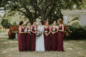Outdoor Bridal Party Portrait Bride in Boho Lace V-Neck Illusion A-Line Wtoo Wedding Dress and White and Burgundy Flowers and Greenery Bouquet, Bridesmaids in Floor Length Burgundy Dresses with White Flower Bouquets | Tampa Bay Wedding Venue Davis Islands Garden Club