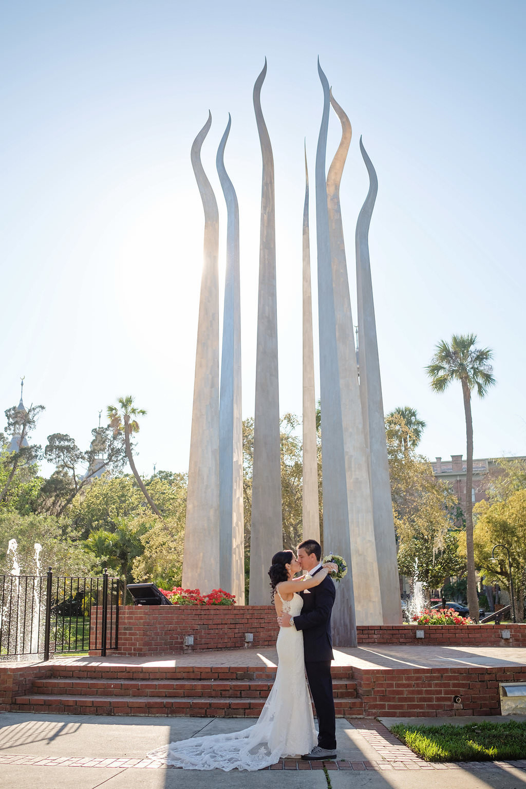 Outdoor Bride and Groom Wedding Portrait Groom in Navy Blue Tuxedo and Bride Wearing Strappy White Lace Wedding Dress with Lace Train in Front of Sculpture | Tampa Bay Wedding Photographer Marc Edwards Photographs