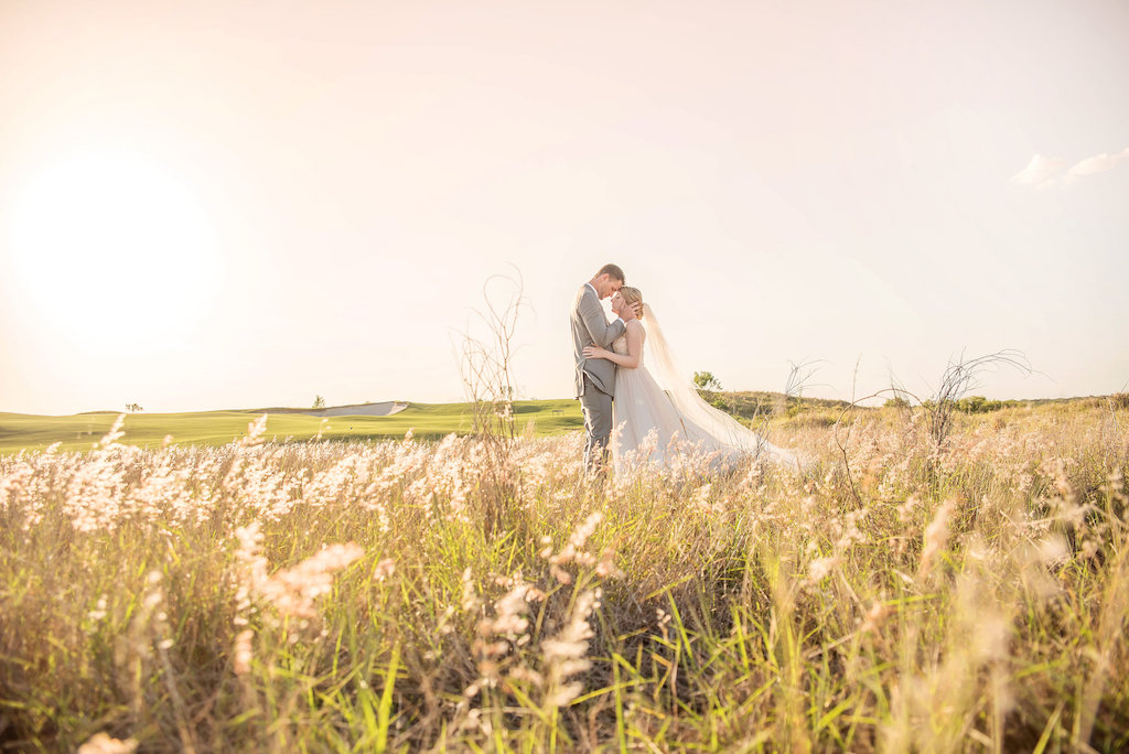 Outdoor Florida Golf Course Bride and Groom Portrait, Bride Wearing V-Neck Plunging Neckline with Floral Lace Overlay Blush Pink Lining and Tank Straps Wedding Dress, Braided Updo and Tulle Floor Length Veil, Groom Wearing Light Grey Suit with Dusty Blue Tie | Marry Me Tampa Bay Photographer Kristen Marie Photography | Marry Me Tampa Bay Hair and Makeup Destiny and Light Hair and Makeup Group